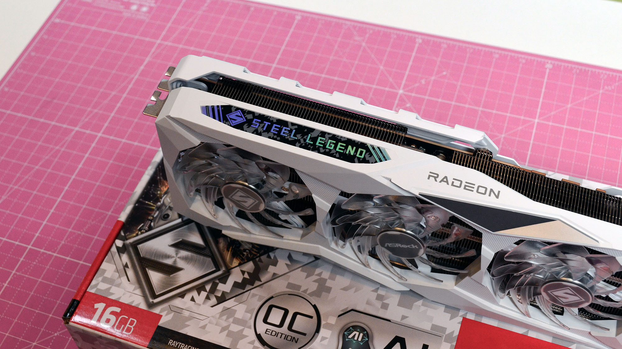 An AMD Radeon RX 7900 GRE from ASRock on a pink desk mat with its retail packaging